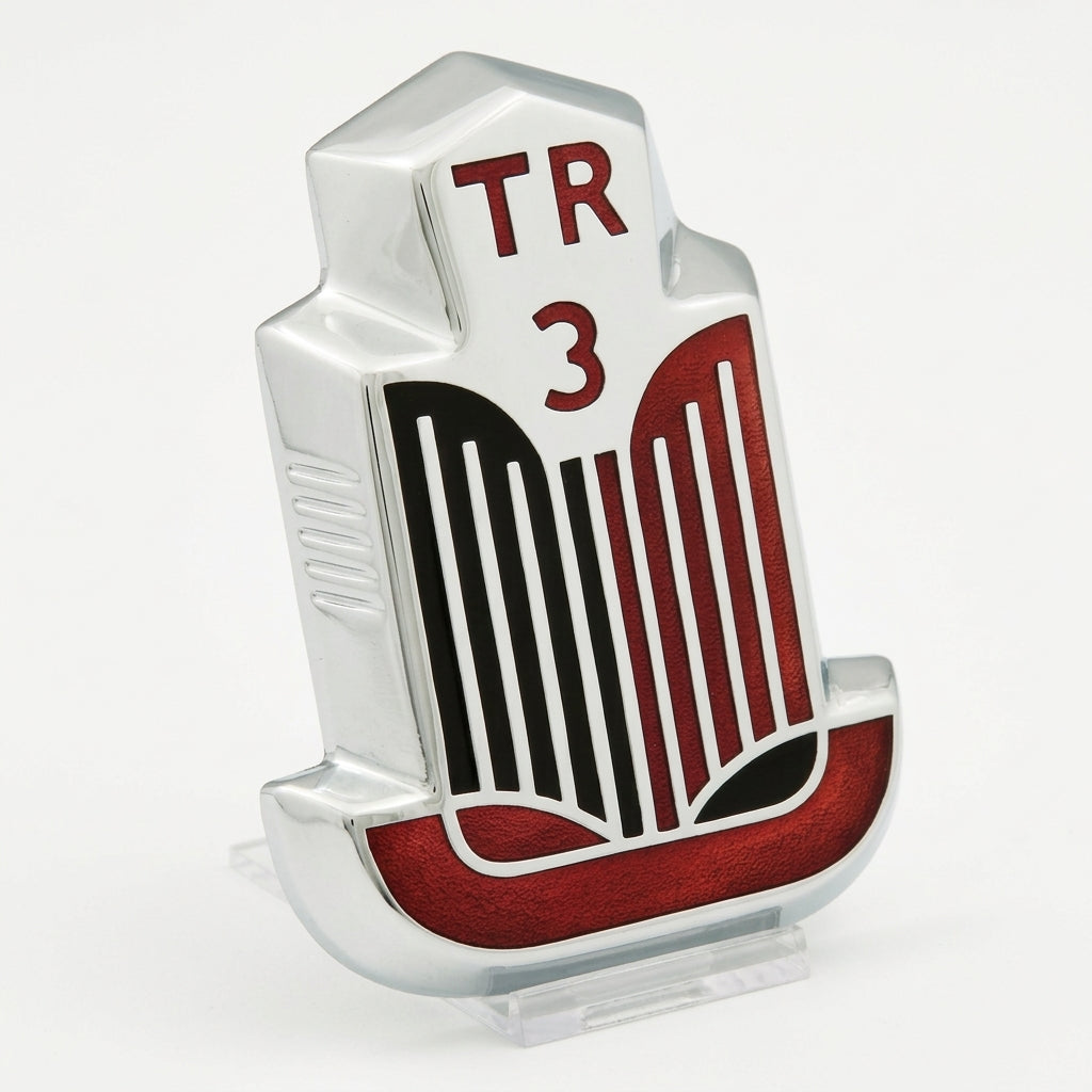 Chrome TR3 bonnet badge with red and black enamel grille, angled studio shot on white