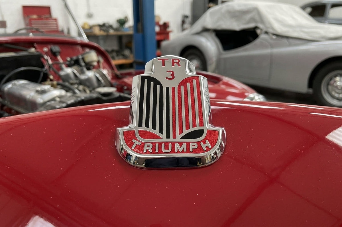 TR3 bonnet badge fitted to a red Triumph, close-up workshop shot