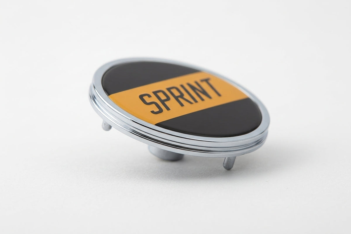 Round chrome-rimmed SPRINT badge angled on white background, studio shot