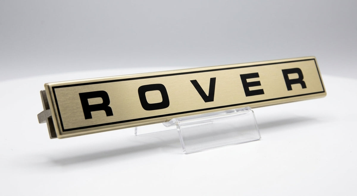 Gold-tone ROVER script badge displayed on a clear stand, studio shot