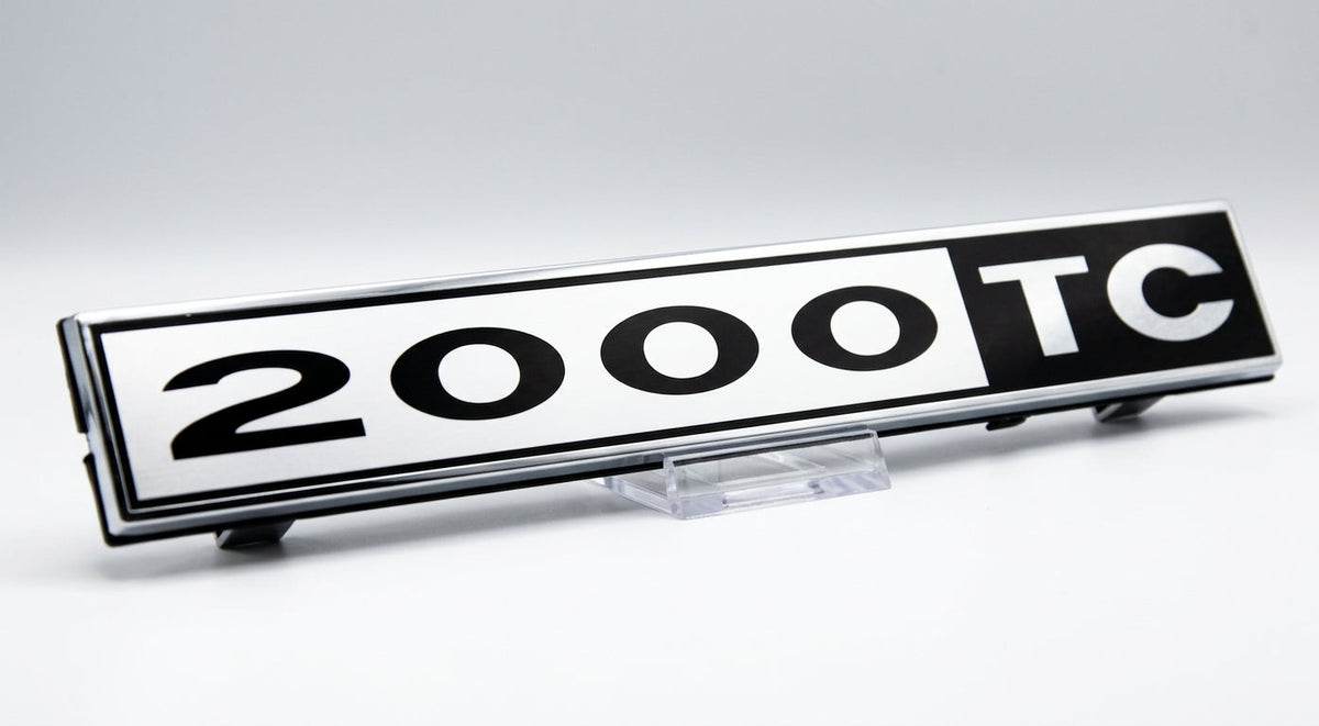 Black and chrome 2000TC badge displayed on a clear stand, studio shot