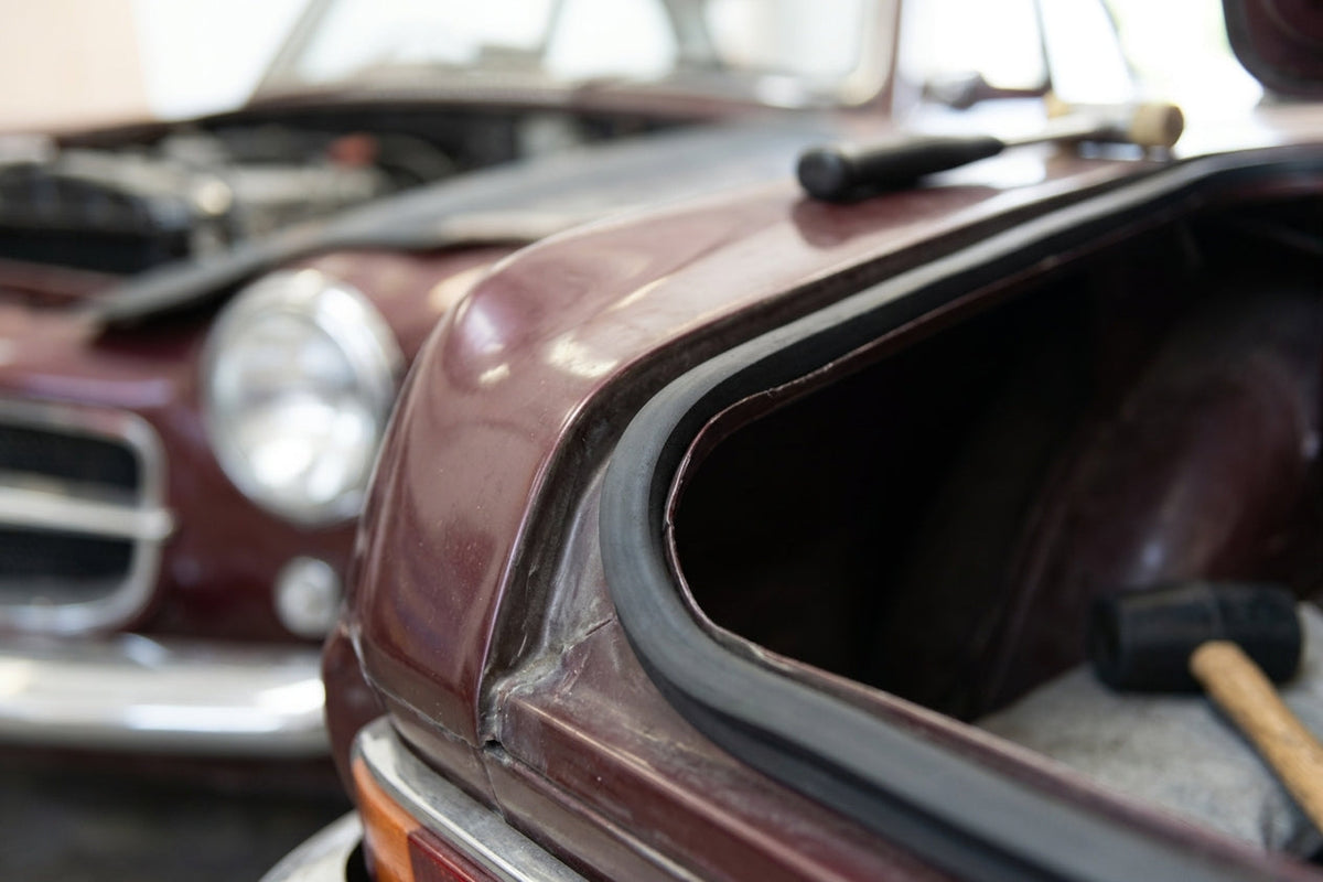 Sponge strip fitted along a maroon classic car's bonnet edge, hammer nearby