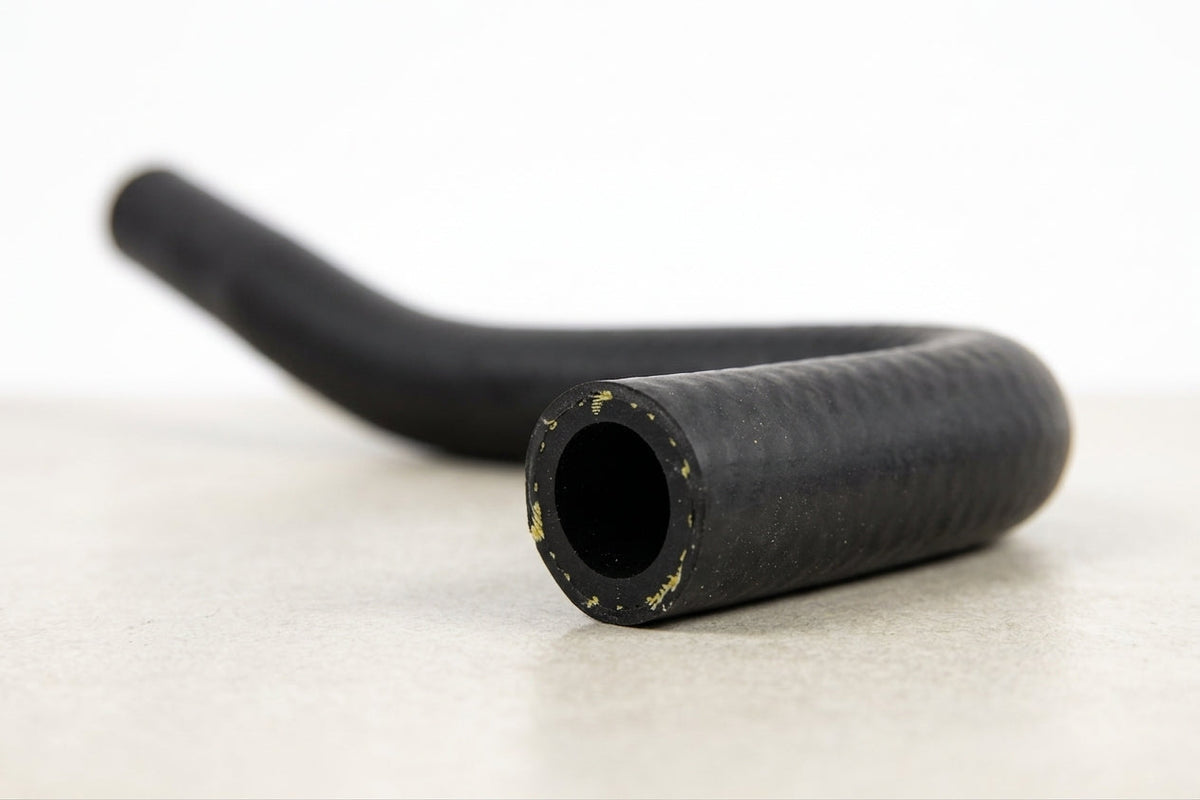 Black ribbed rubber heater hose with a bend, studio shot on a light surface