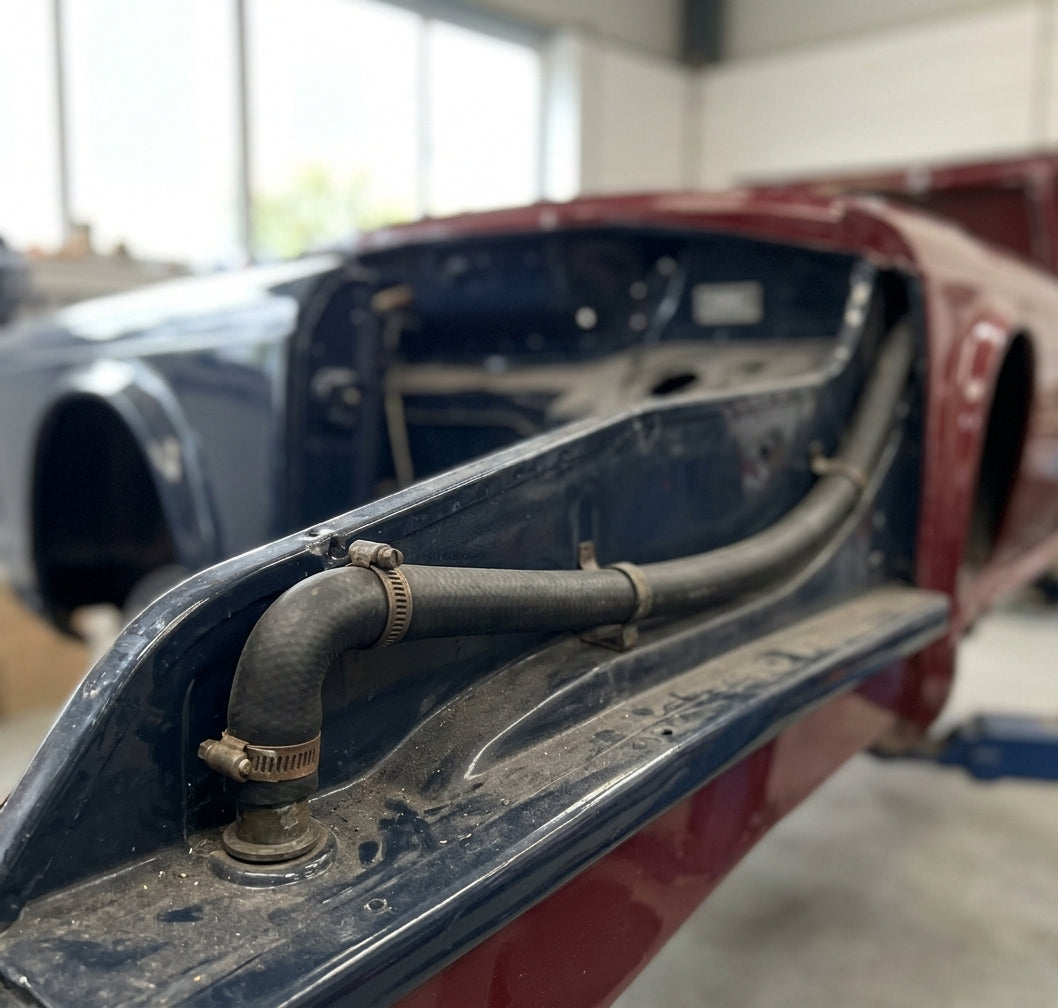Black hose clipped along the scuttle drain of a maroon bodyshell, second shell behind in the workshop