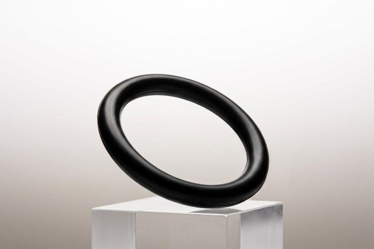 Black nitrile O-ring balanced on a clear plinth, studio shot