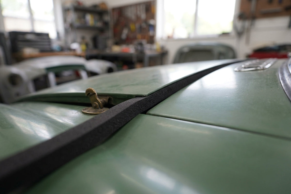 Thin black foam strip fitted along a green classic car's bonnet centre seam
