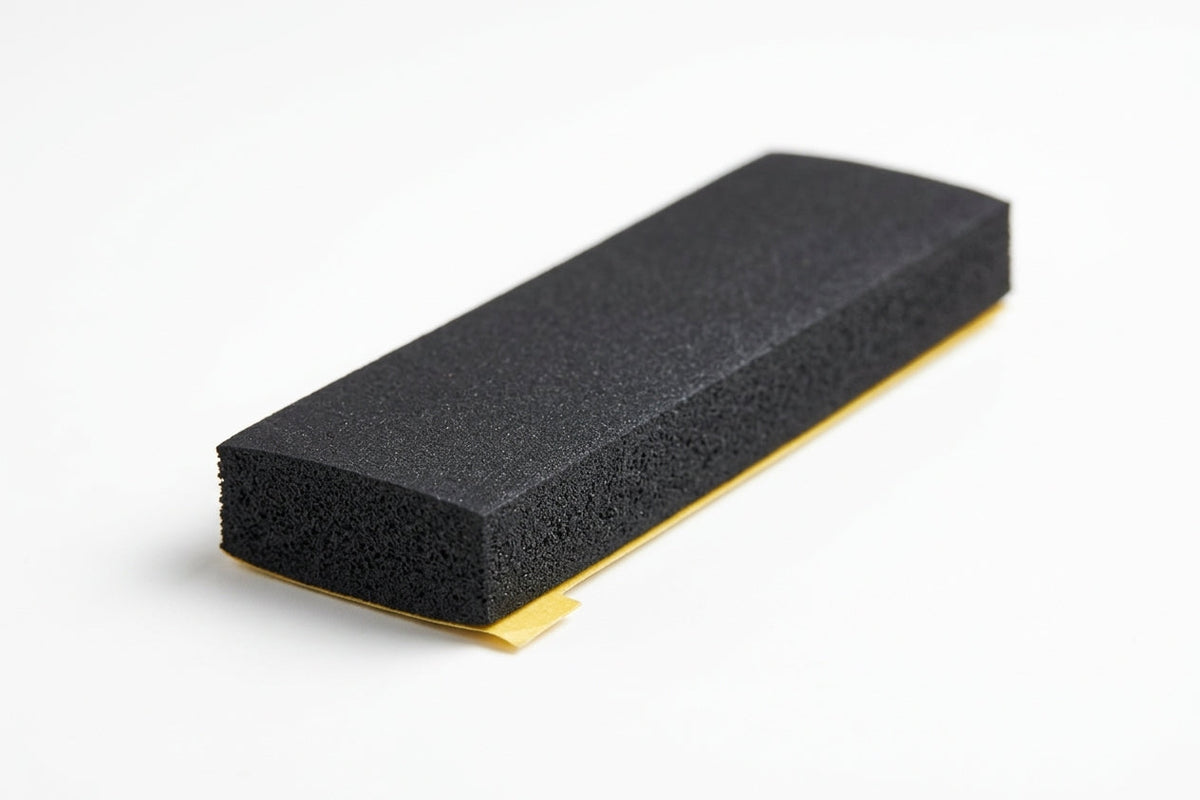 Black sponge strip block with yellow adhesive backing peeled out from underneath, studio shot