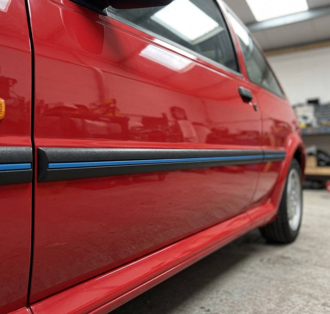 Blue-striped black moulding along the mid-door of a red Fiesta, car facing left, close three-quarter view