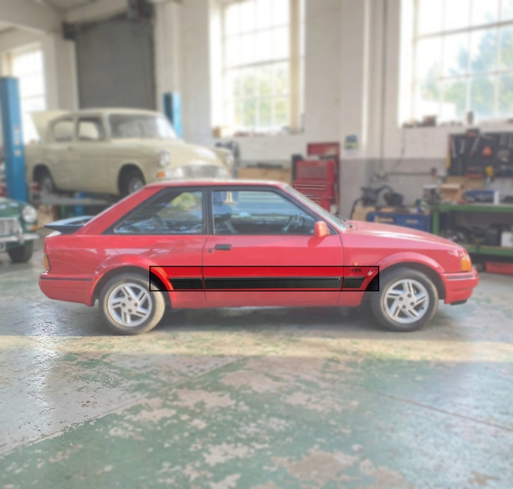 Red Escort XR3i viewed side-on in a workshop, black mouldings running low along both doors and sills