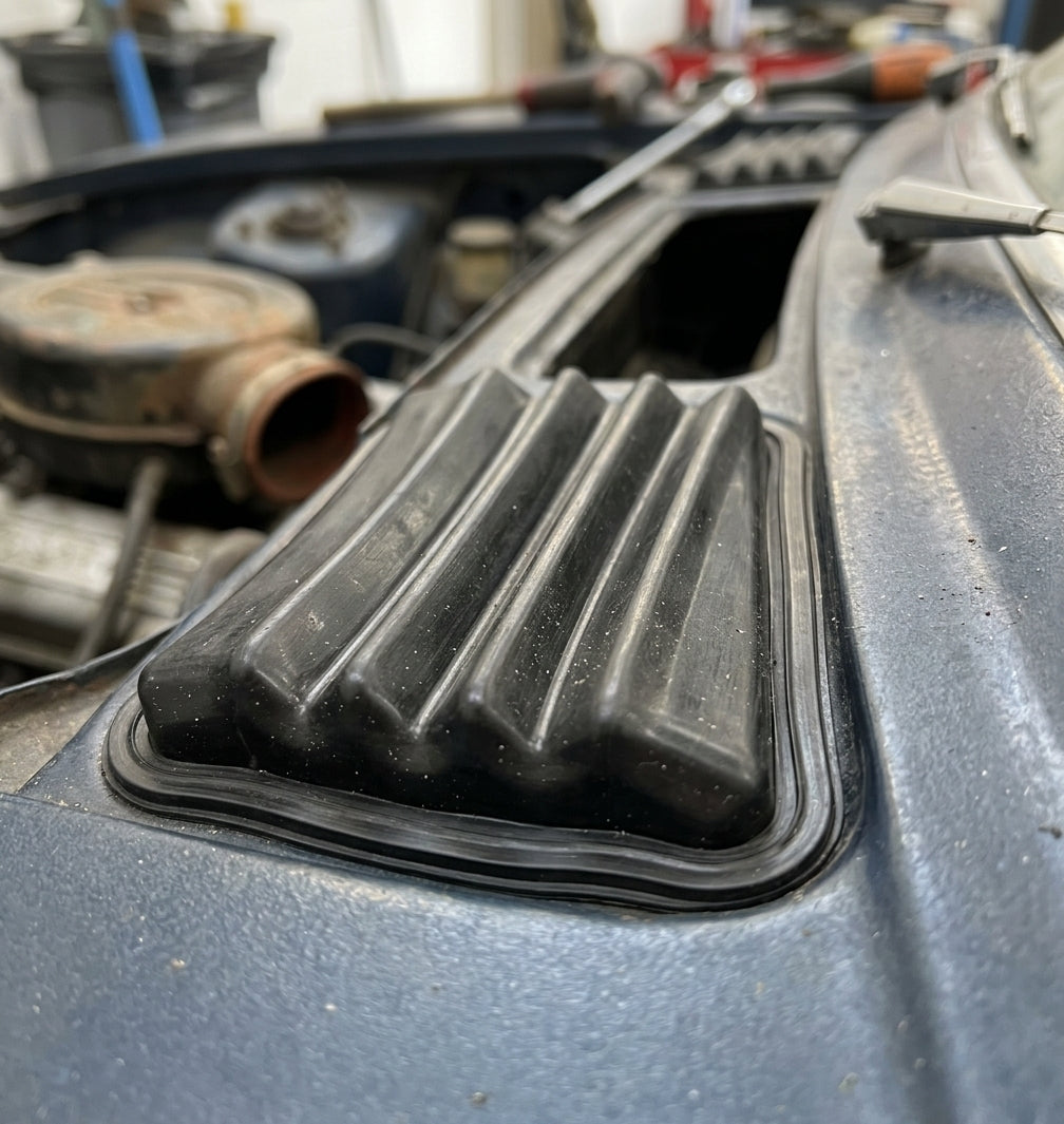 Ribbed rubber air intake gaiter fitted to a Triumph Stag scuttle panel, engine bay behind