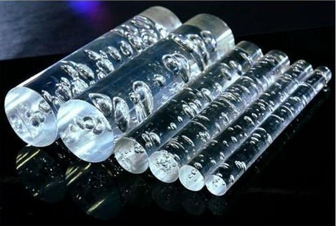 Six clear bubble acrylic rods on a black reflective surface, trapped bubbles catching the light