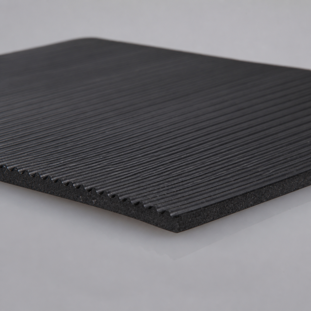 Black fluted rubber matting on a pale surface, fine parallel ribs running across the face with one corner lifted