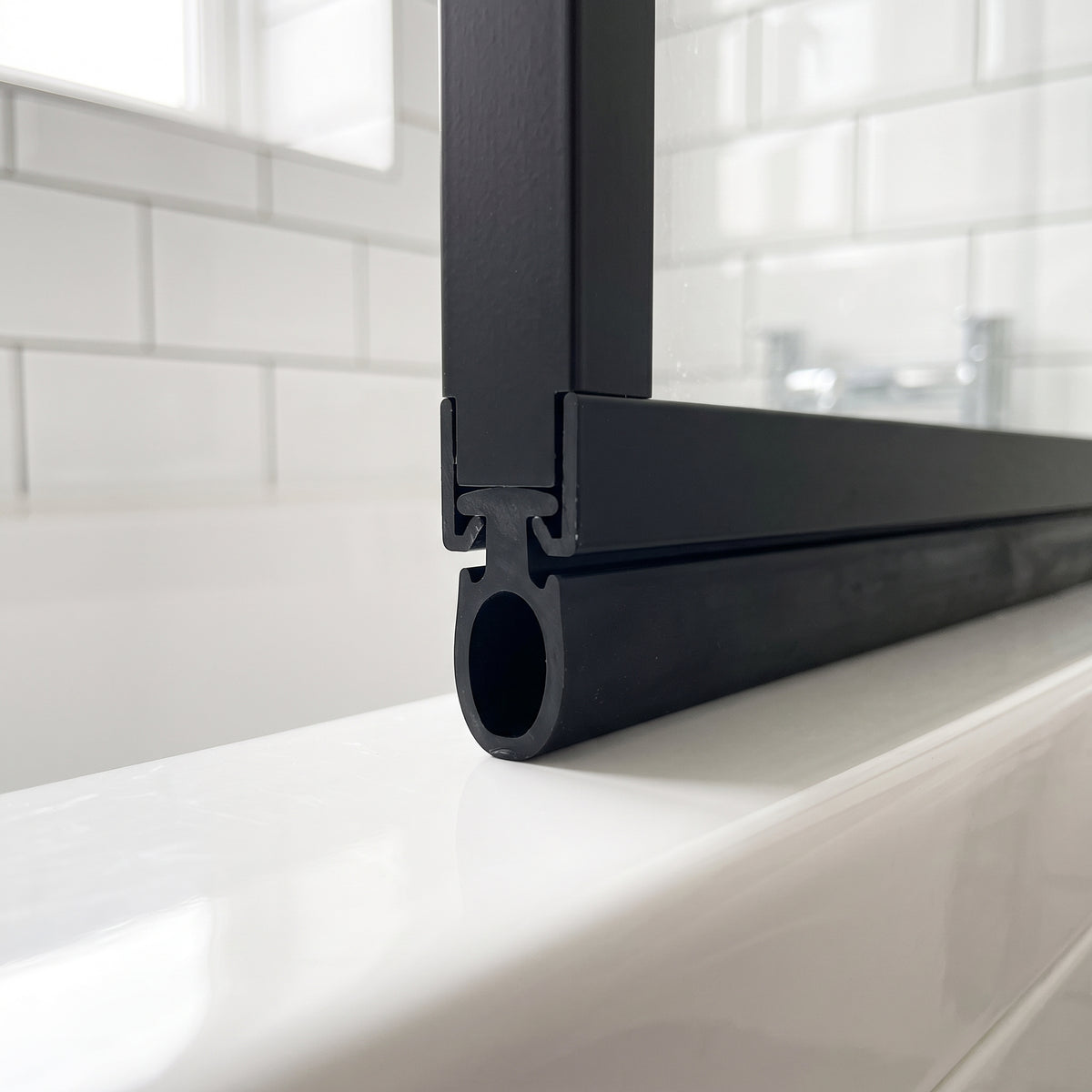 Black 5.5mm T-head bifold seal slotted into the channel of a black-framed bath screen, hollow bulb sealing the gap to the bath