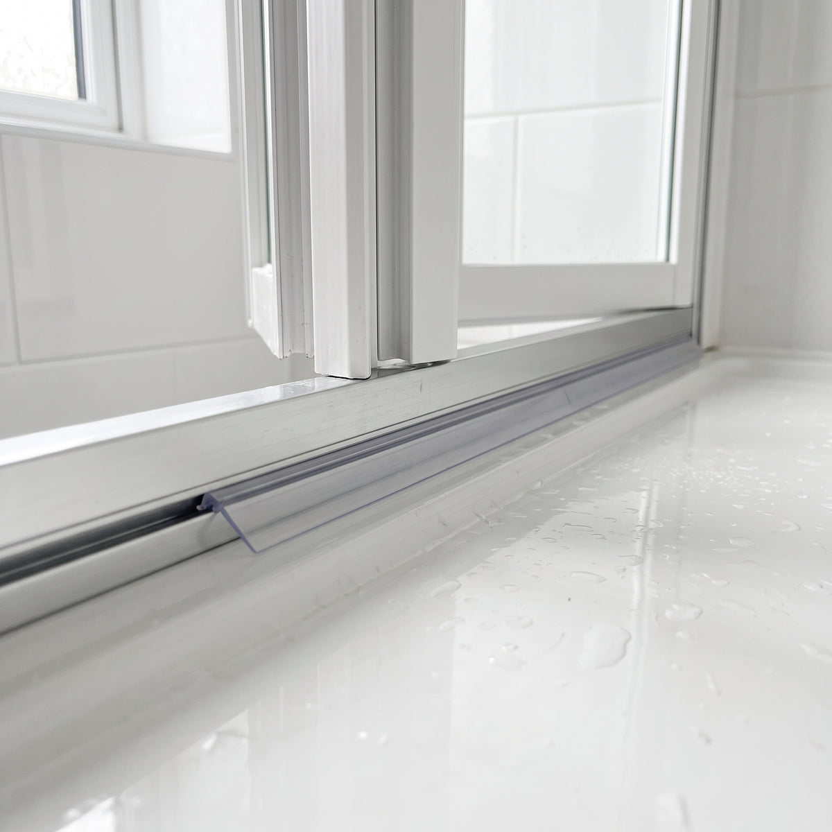Slim clear blade seal in a narrow aluminium rail beneath a white bifold door, wet tray below