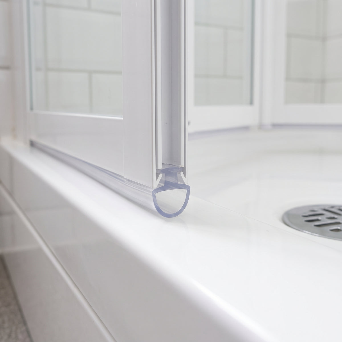Clear seal with a rounded hollow foot at the base of a white bifold door, on a white tray with chrome waste