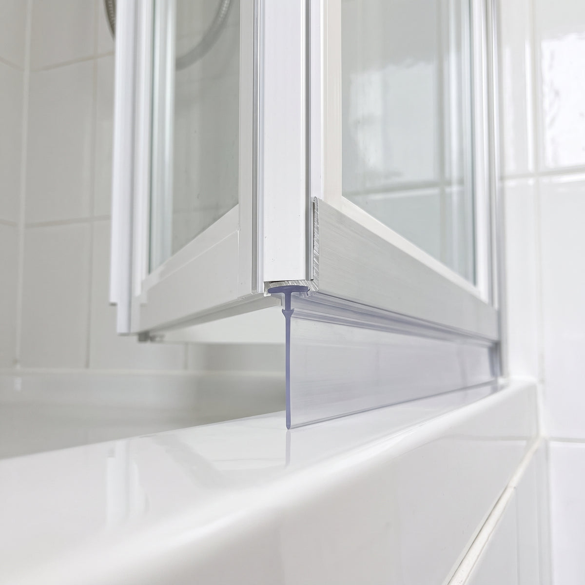 Clear blade seal under the bottom rail of a white bifold bath screen, meeting the glossy tray edge