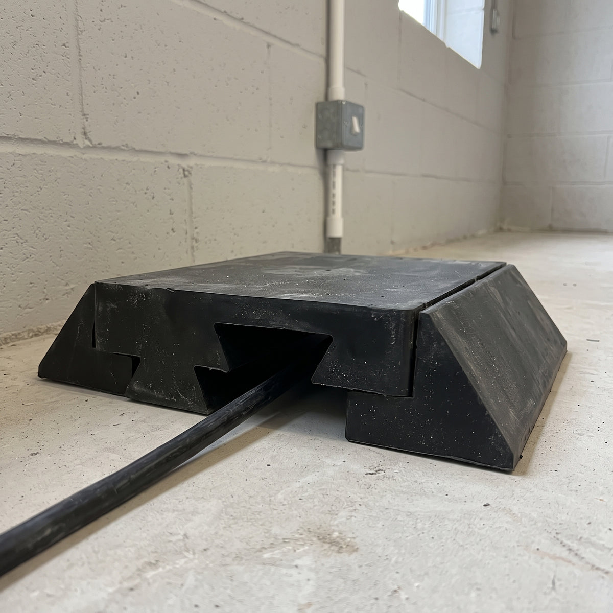 Black ramp centre module on a concrete floor by a block wall, a cable running out from under its interlocking end