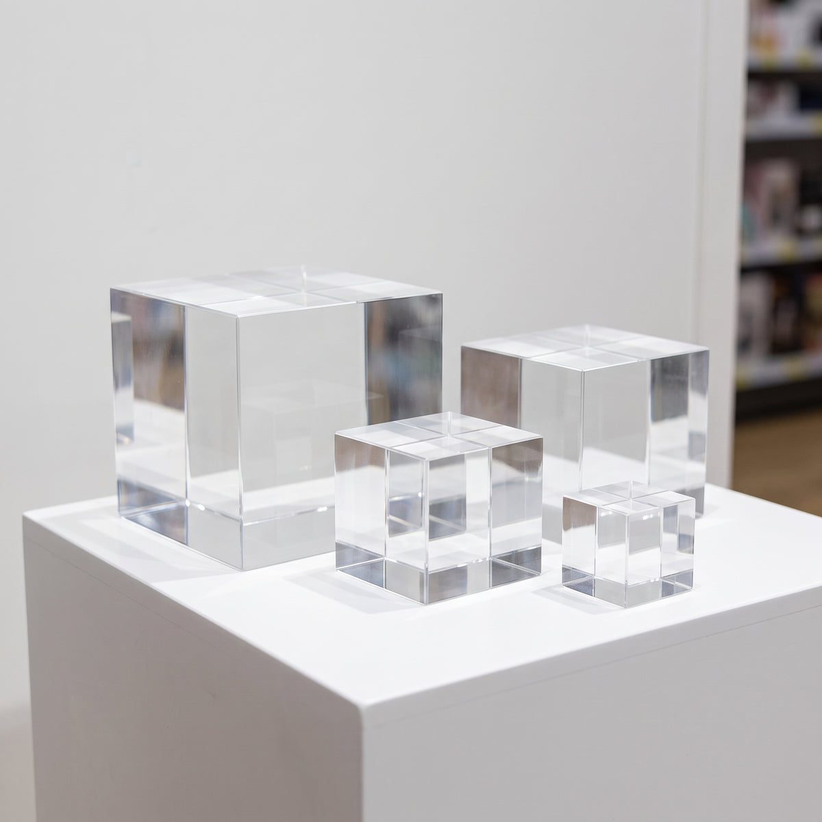 Four clear cast acrylic cubes in graduated sizes standing on a white display plinth, light catching their polished edges