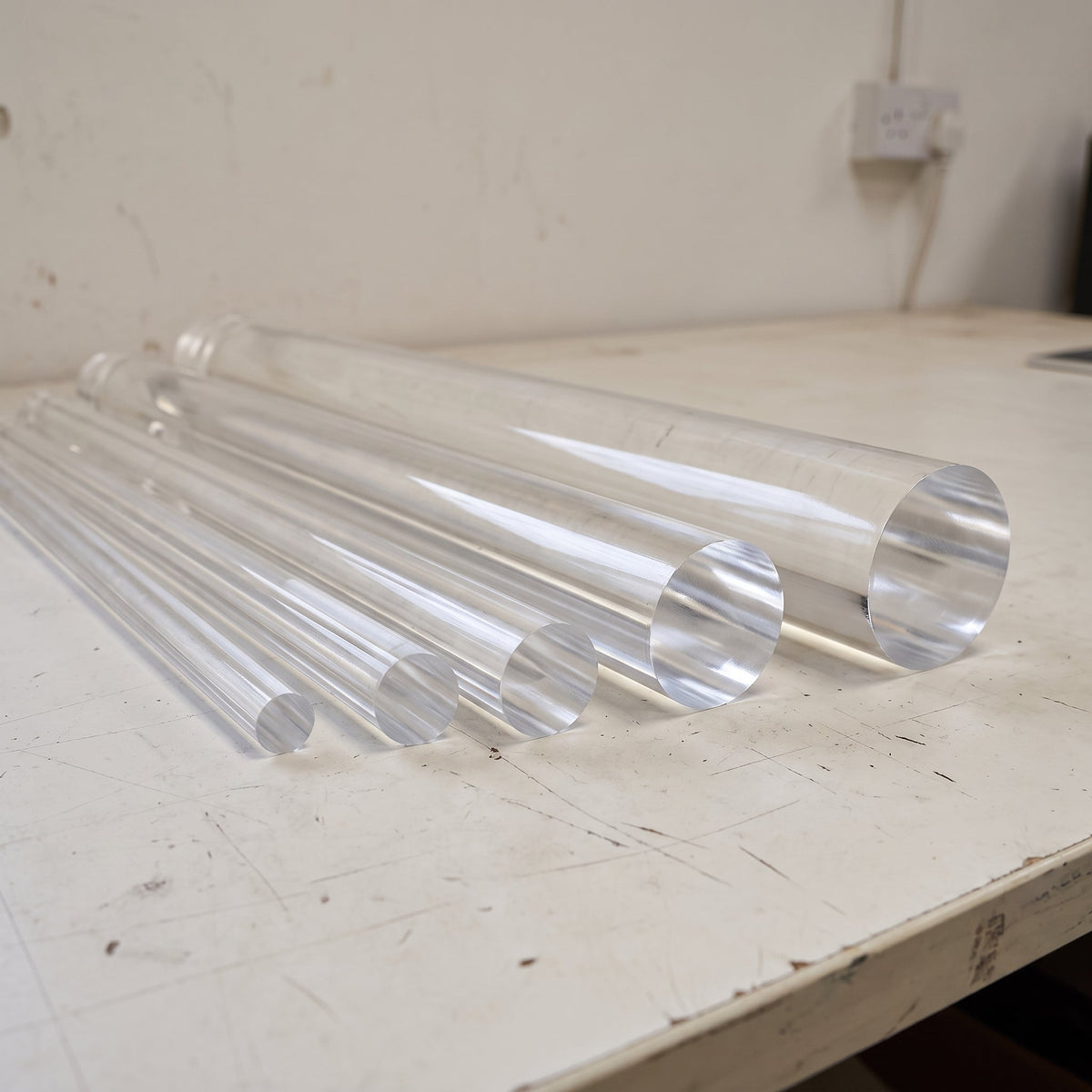 Clear acrylic rods of several diameters fanned across a scuffed white bench, round ends towards the lens