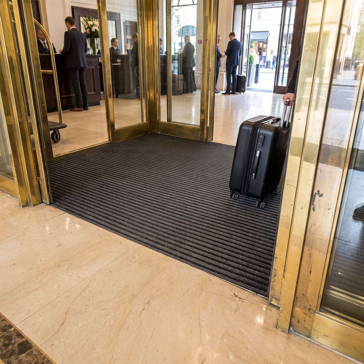 Made-to-measure ribbed entrance mat with carpet inserts fitted at a hotel lobby entrance with a wheeled suitcase rolling over it