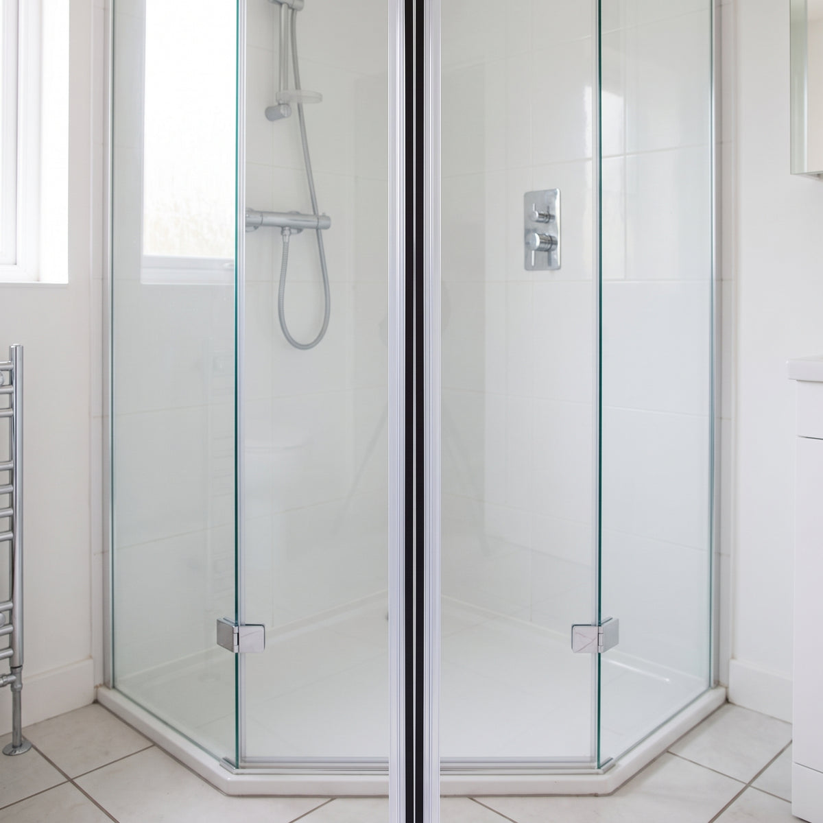 Pentagonal glass shower enclosure closed, a dark magnetic seal line running the full height of the join
