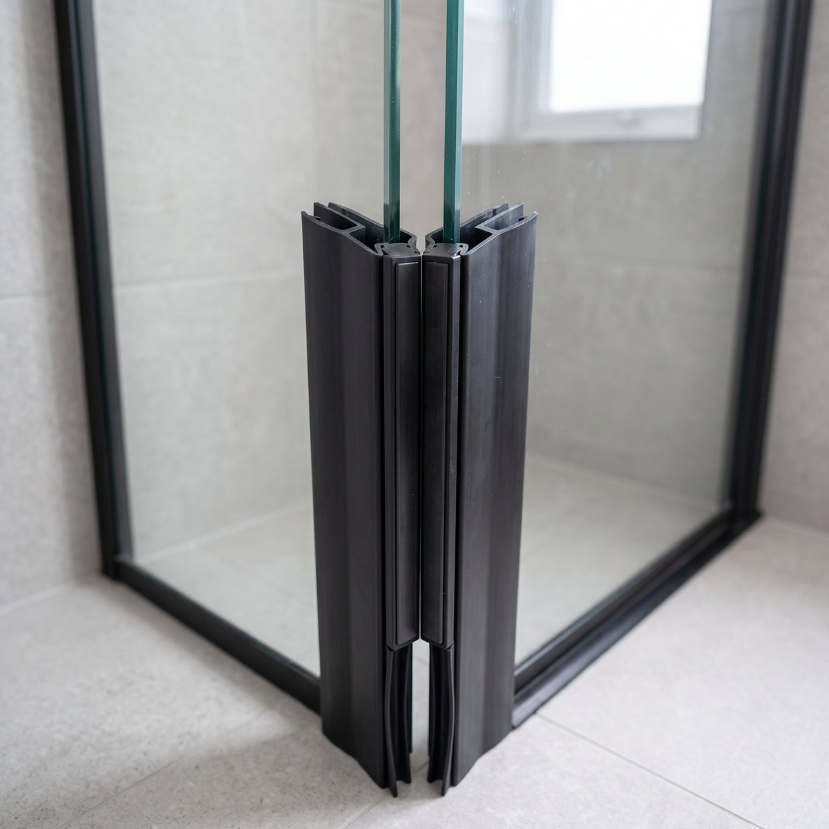 Black seals meeting at the 90 degree corner of a black-framed glass enclosure, grey tiles behind