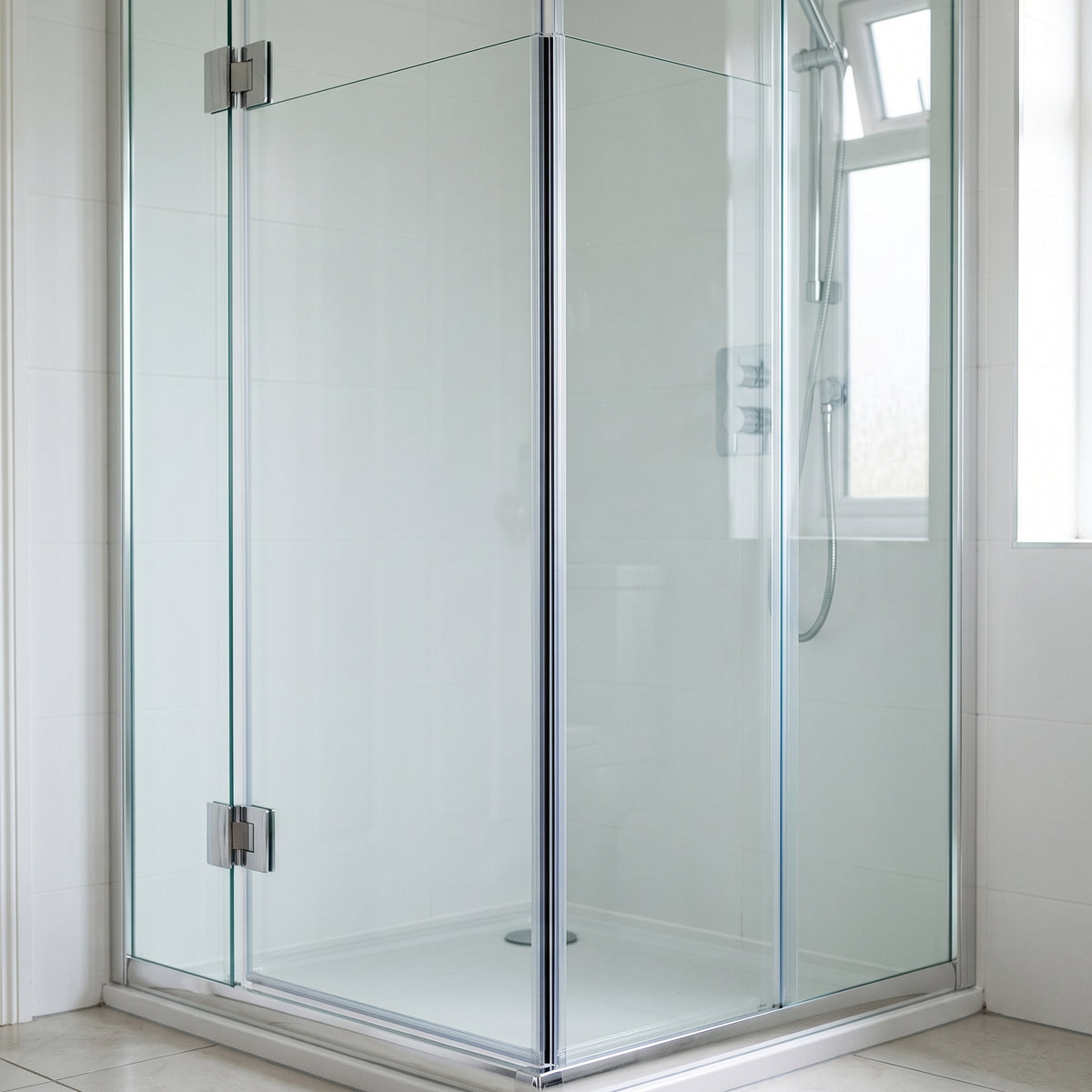 Frameless glass shower enclosure with chrome hinges in a white bathroom, seal not visible at this distance