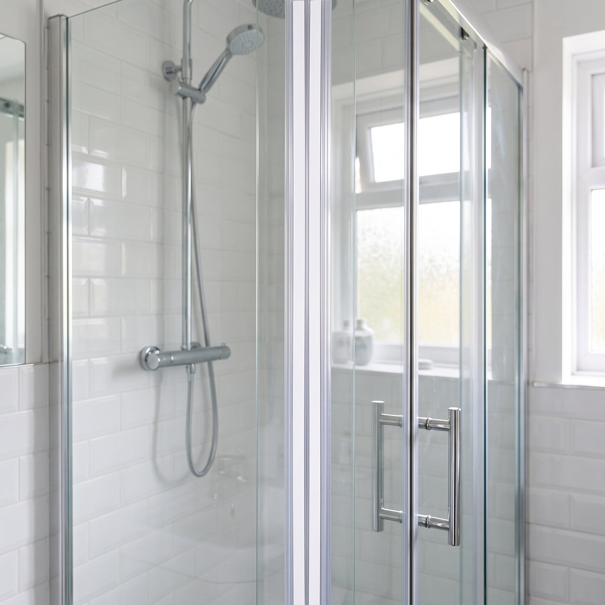Bifold glass shower door closed in a white metro-tiled bathroom, a pale seal line down the join