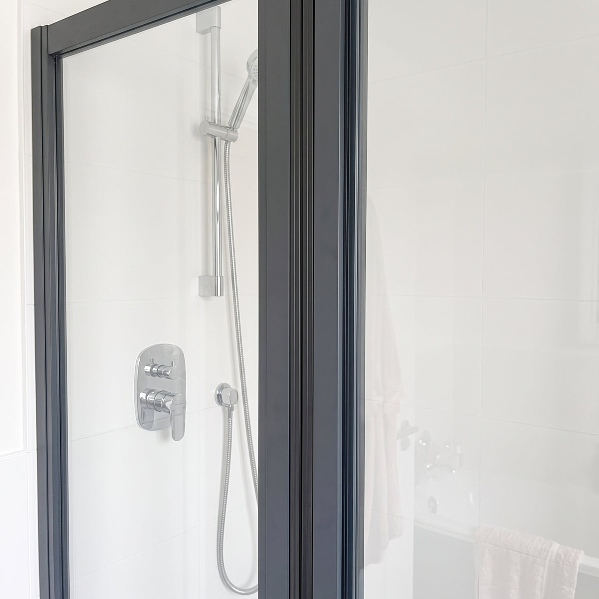 Dark-framed shower door closed against a fixed panel, chrome mixer and riser rail behind, white tiled walls