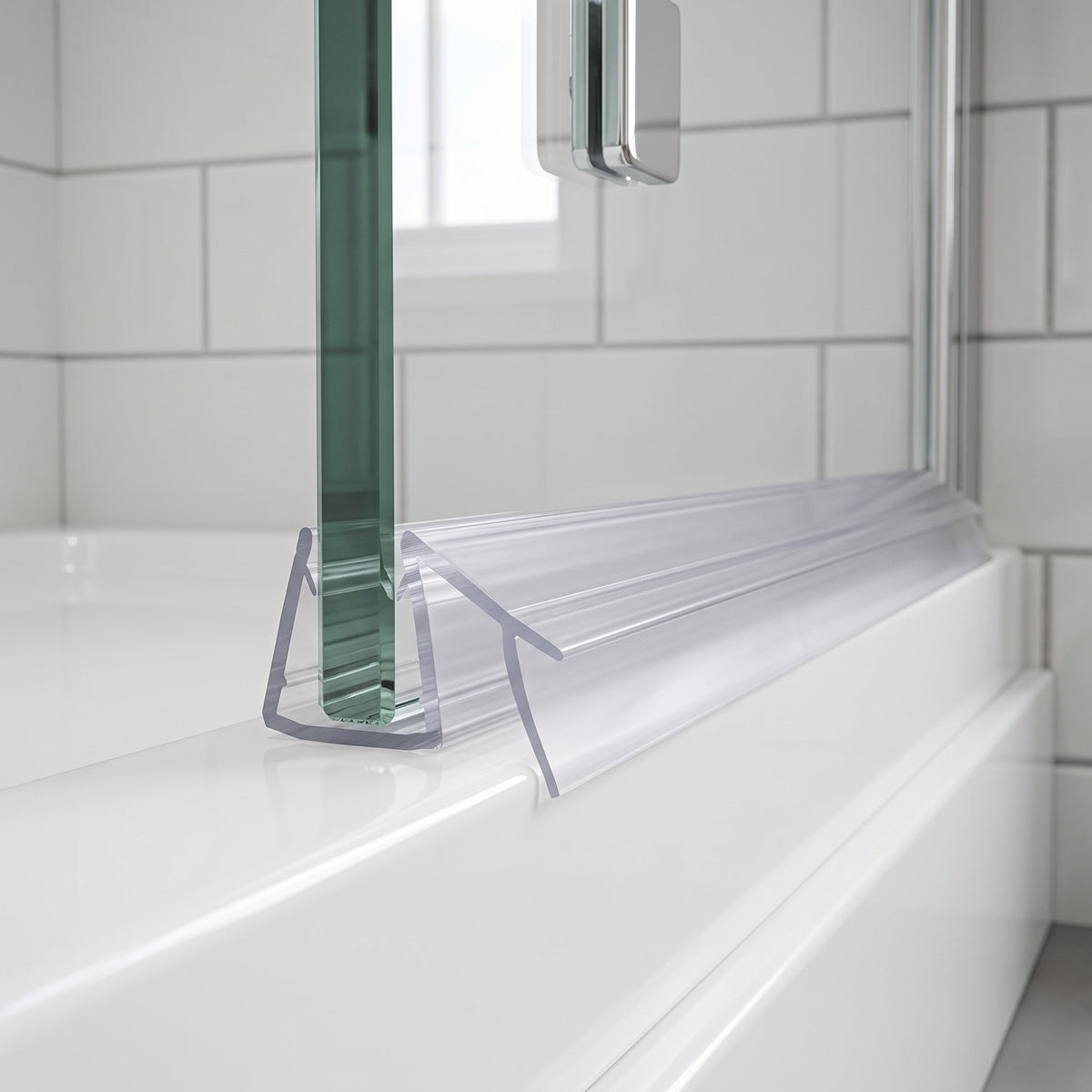 Clear seal with two angled blades at the foot of a glass bath screen on a white bath, metro tiles