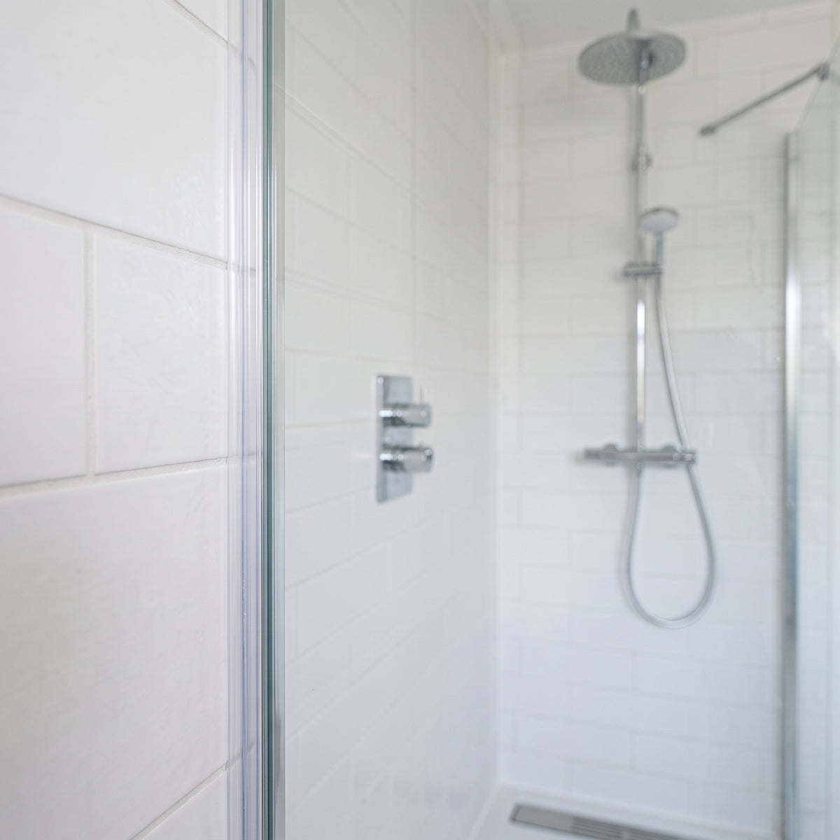Glass shower screen in a white-tiled bathroom with a chrome riser rail, seal not visible here