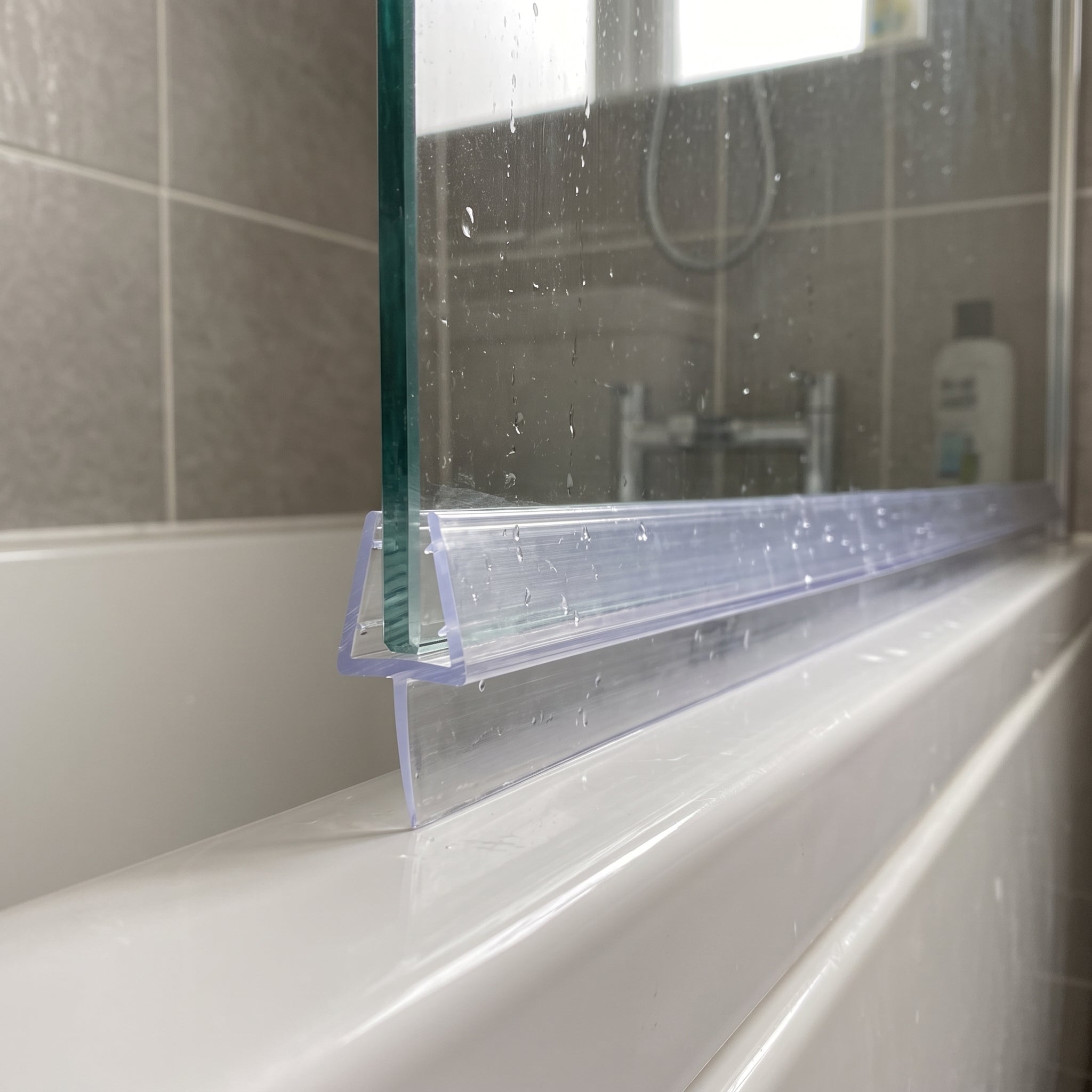 Tapered shower screen seal pushed onto the bottom edge of 6-8mm glass, clear fin tapering from 15mm to 5mm to close an uneven gap to the shower tray