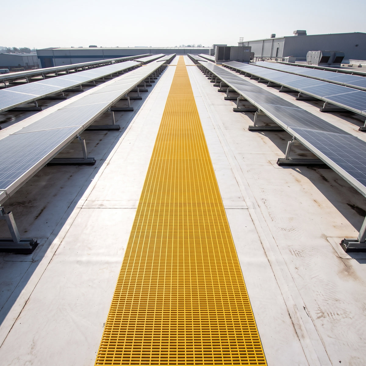 Yellow open-lattice walkway matting as a long straight run between rows of solar panels on a pale membrane roof