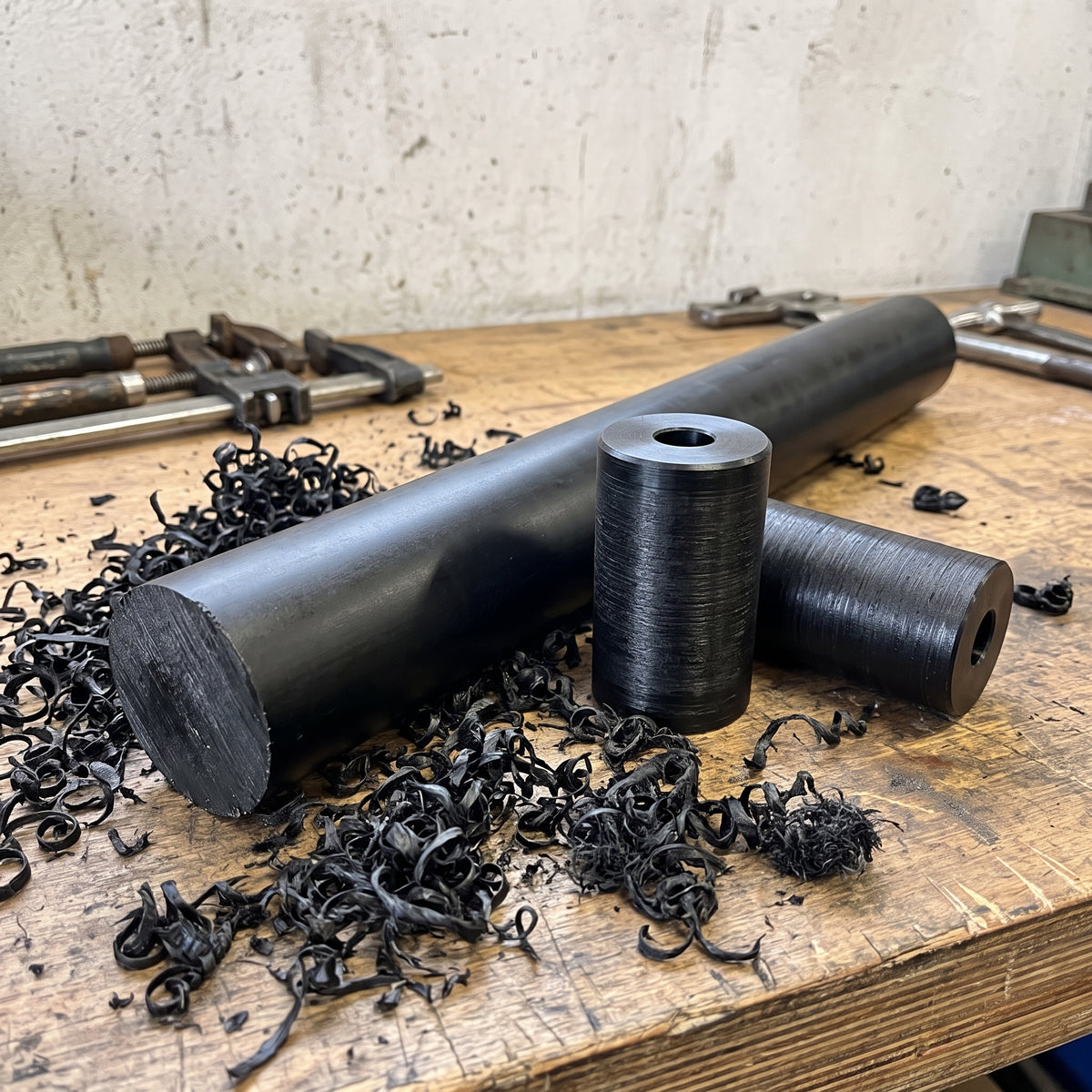 Black UHMWPE rod on a workshop bench beside two turned black rollers cut from it, black swarf around