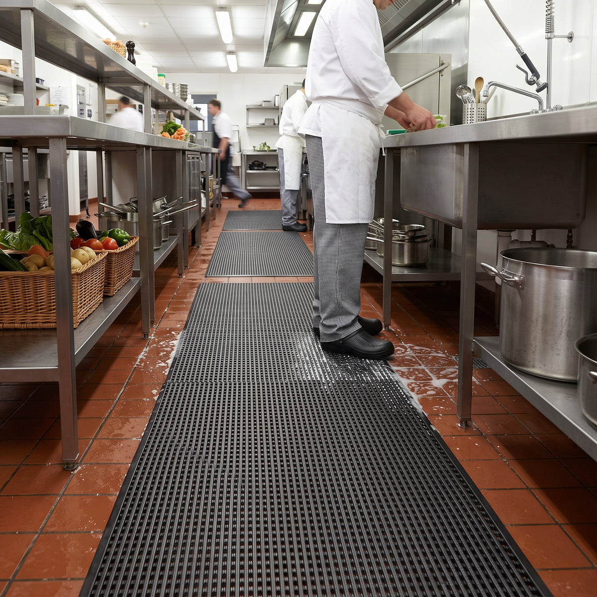 Black open mesh PVC grip matting laid down the wash-up aisle of a commercial kitchen with water draining through