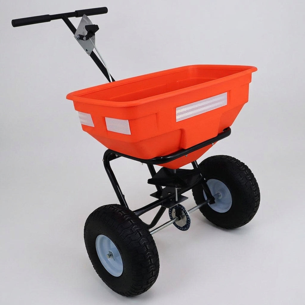 Orange hopper salt spreader on a steel frame with two pneumatic wheels, photographed on a plain grey background