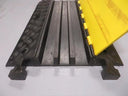 Close-up of three ribbed cable channels with the yellow hinged lid open, on a floor