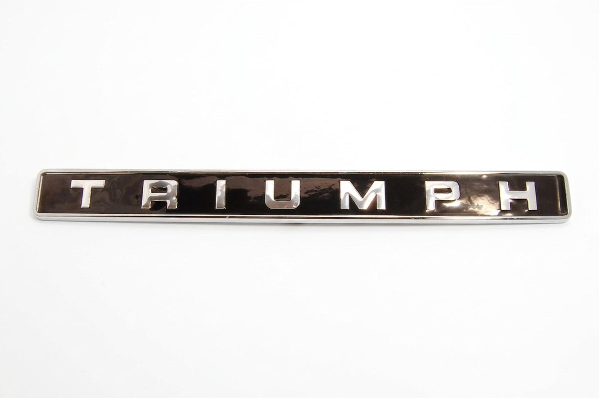 Chrome TRIUMPH badge shown alone on a plain studio background