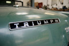 Chrome TRIUMPH badge fitted to the bonnet of a green classic car