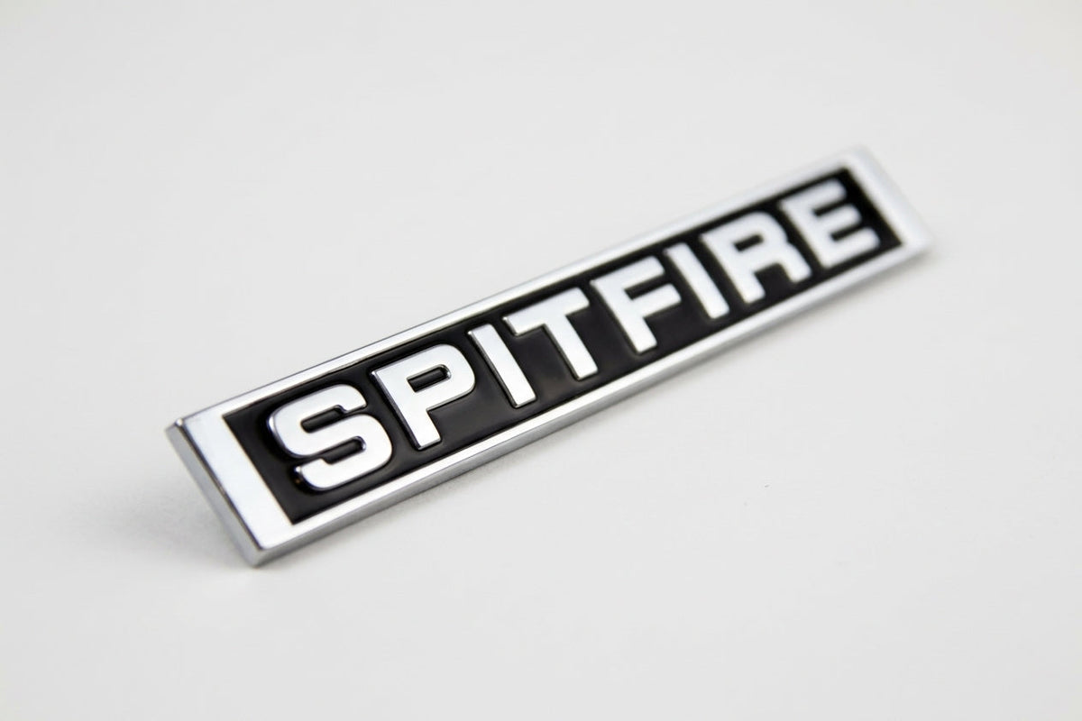 Black enamelled SPITFIRE badge with chrome block lettering and chrome surround, angled on white