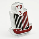 Chrome TR3 bonnet badge with red and black enamel grille, angled studio shot on white