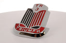 Chrome bonnet badge with black and red enamel and TRIUMPH script, studio shot