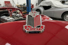 TR3 bonnet badge fitted to a red Triumph, close-up workshop shot