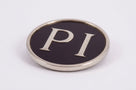 Round chrome-rimmed black badge reading PI, studio shot on white background