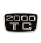 Chrome and black enamel badge reading 2000 TC, studio shot on white background