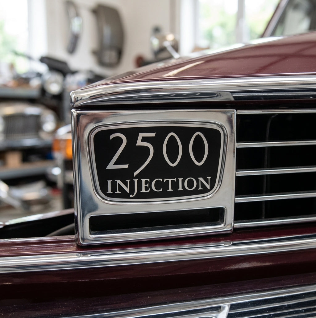 2500 INJECTION badge in the chrome grille surround of a maroon car, workshop blurred behind