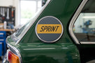 Round grey and yellow SPRINT pillar badge fitted to a green car's B-pillar