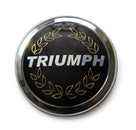Round chrome laurel wreath badge with TRIUMPH lettering, studio shot on white