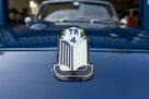 TR4 bonnet badge fitted to a dark blue Triumph, front-on view