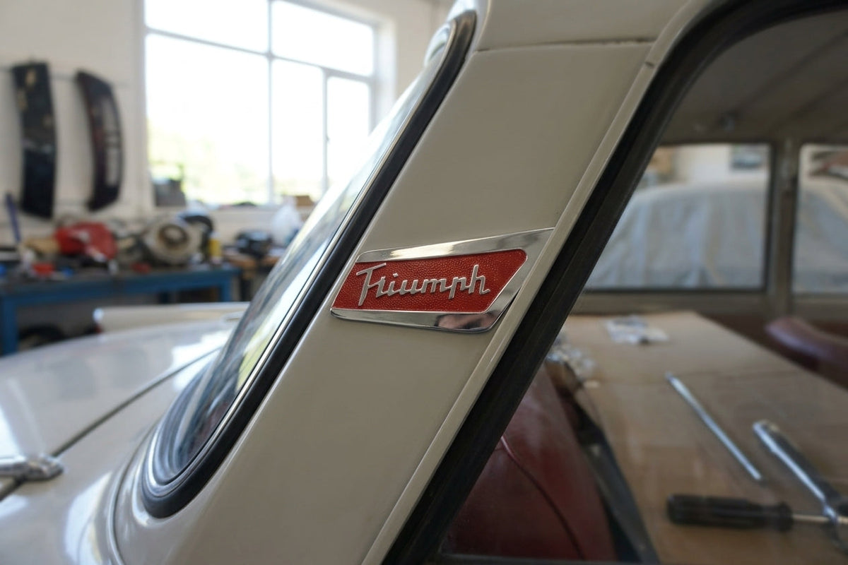 Red and chrome Triumph pillar badge fitted to a white car's rear pillar